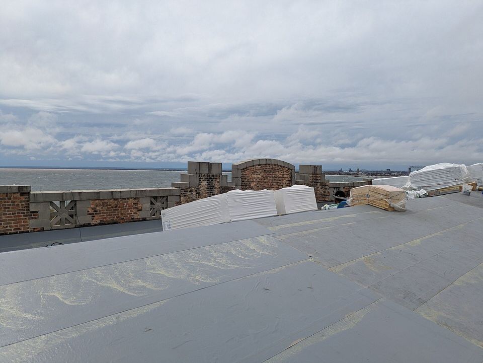 Flat roof with fresh gray membrane and stacked insulation boards beside a brick parapet