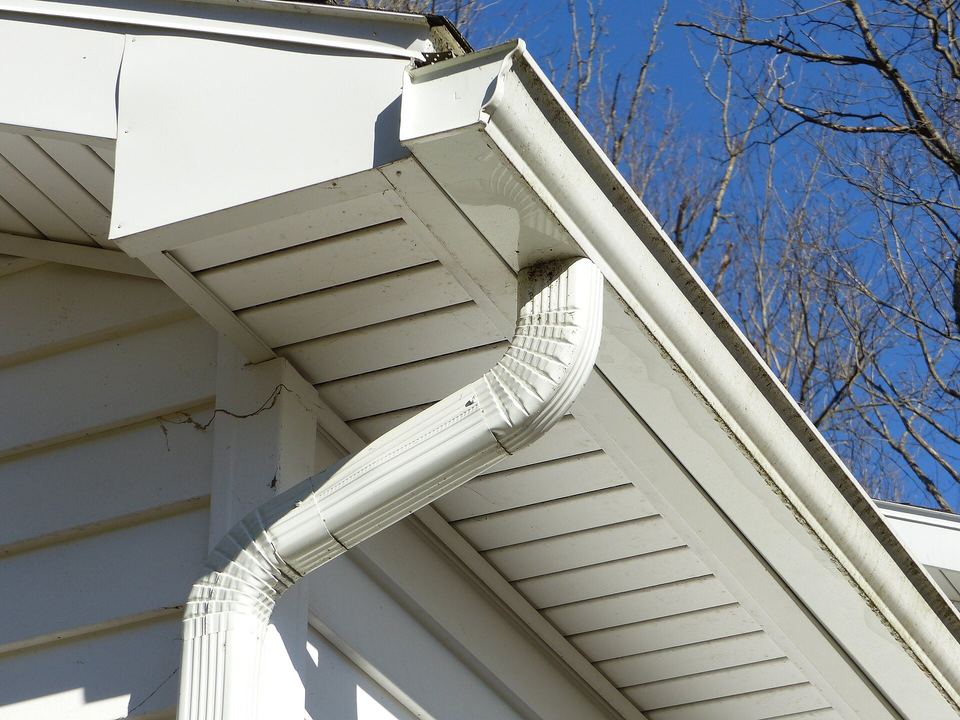 White seamless aluminum gutter and downspout under a house eave against blue sky