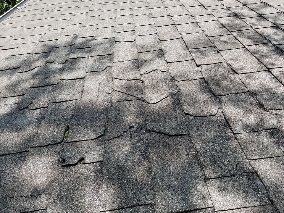 Close-up of cracked and torn gray asphalt shingles damaged during a thunderstorm