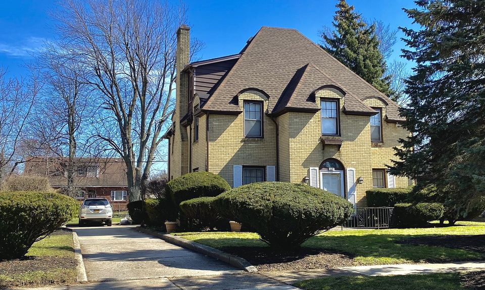 Yellow brick two-story house with a steep brown architectural shingle roof and blue sky
