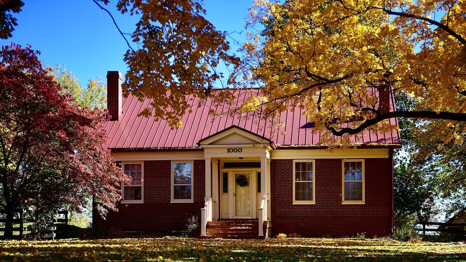 Red brick house with a red standing-seam metal roof among bright autumn trees