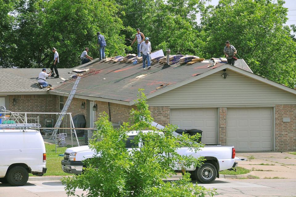 Several roofers working across the roof of a ranch house with an attached garage