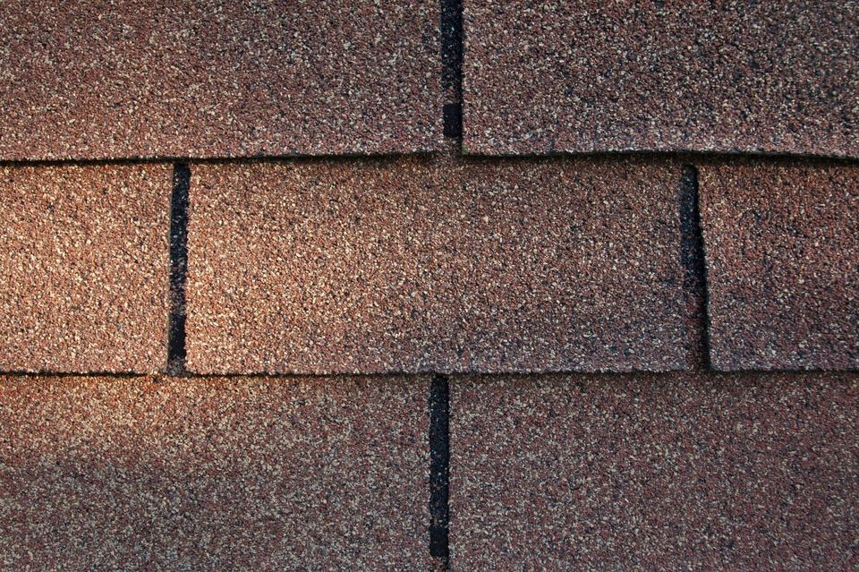 Close-up texture of brown asphalt roof shingles with a granular surface