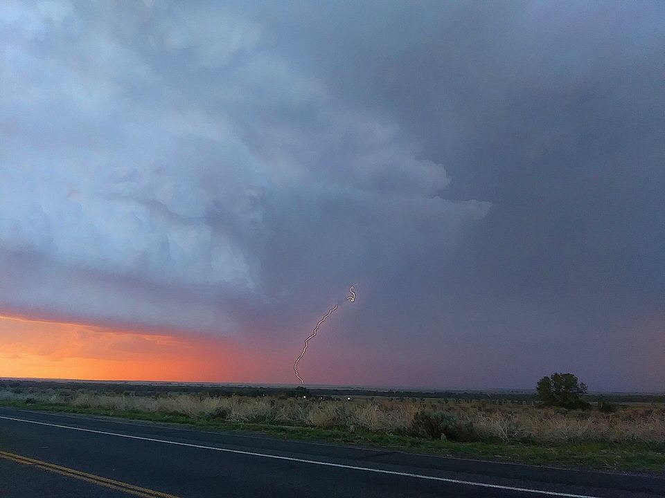 Lightning bolt and a dark shelf cloud sweeping over flat open plains at dusk